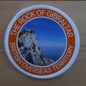 May include: A round, orange and white patch with the text "The Rock of Gibraltar British Overseas Territory" surrounding a photo of a rocky cliff with a building on top.
