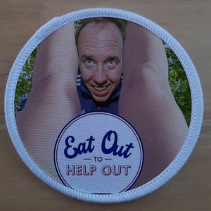 Op de afbeelding: Een ronde witte patch met een blauwe en rode cirkel in het midden. De cirkel heeft de tekst "Eat Out to Help Out" in blauwe en rode letters.