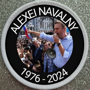 May include: A circular embroidered patch with a white border and a black background. The centre features a photograph of Alexei Navalny speaking into a megaphone at a rally. The text ALEXEI NAVALNY is at the top and 1976 - 2024 is at the bottom.