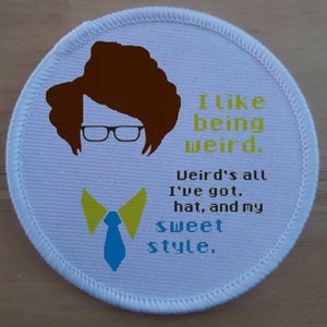 May include: White round patch with a brown cartoon figure wearing glasses and a blue tie with yellow bowtie. The text reads "I like being weird. Weird's all I've got. hat, and my sweet style."