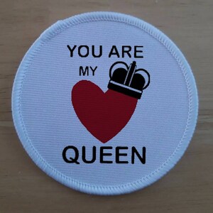 Könnte beinhalten: Runder Stoff-Patch in Weiß mit schwarzem Text "You are my Queen" mit einem roten Herzen und einer schwarzen Krone auf dem Herzen.