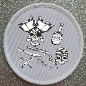 May include: A white round patch with a black and white illustration of a pirate skull wearing an eye patch and a tricorn hat, a bottle of rum, a pistol, a sword, crossed bones, and a skeleton hand.