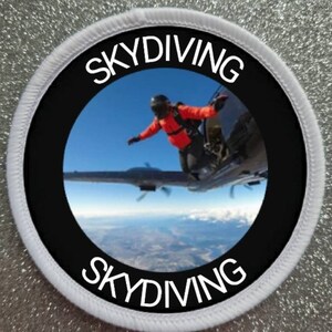 May include: White round patch with black border and white text "SKYDIVING" on top and bottom. The centre of the patch features a photo of a skydiver exiting an aeroplane.