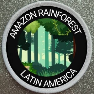 May include: A white round patch with black text that reads "Amazon Rainforest Latin America". The centre of the patch features a black circle with a green and blue illustration of a rainforest.