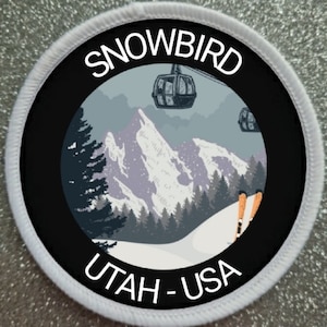 May include: White round patch with a black border and a graphic of a snowy mountain scene with ski lifts and skiers. The text "SNOWBIRD UTAH - USA" is printed in white on the patch.