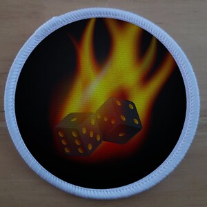 May include: Two black dice with yellow dots are set against a background of orange and yellow flames. The dice are in focus and the flames are blurred.