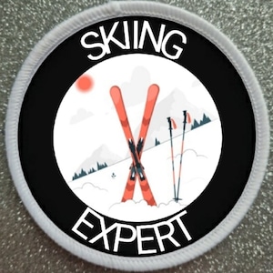 Könnte beinhalten: Ein runder weißer und schwarzer Patch mit dem Text "Skiing Expert" in weißen Buchstaben. Die Mitte des Patches zeigt einen weißen Hintergrund mit einer roten und weißen Illustration von Skiern und Skistöcken.