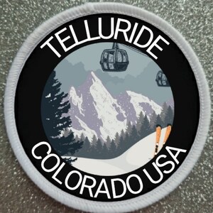 May include: Circular patch with a black center featuring a mountain scene with ski lifts, trees, and the text "TELLURIDE COLORADO USA" in white. The patch has a white border.