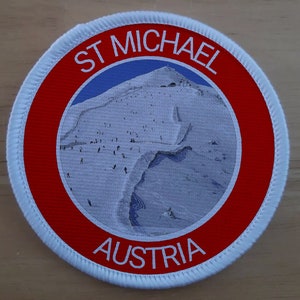 Könnte beinhalten: Ein runder weißer Patch mit roten und blauen Akzenten. Der Patch zeigt eine schneebedeckte Berglandschaft mit dem Text "ST MICHAEL AUSTRIA" in weiß.