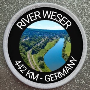 以下が含まれることがあります： 「River Weser 442 KM - Germany」というテキストと、緑の風景の中を蛇行する川の写真が描かれた白黒の丸いパッチです。