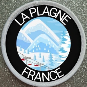 May include: A white and black round patch with the text "LA PLAGNE FRANCE" and a blue and white illustration of a snowy mountain scene with a ski lift.