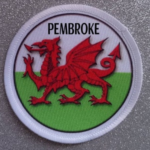 Peut inclure: Un écusson circulaire blanc avec un dragon rouge sur un fond vert et blanc. Le texte "PEMBROKE" est imprimé en noir en haut de l'écusson.