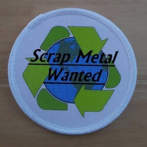 May include: White round patch with a green recycling symbol and a blue globe in the centre. The text "Scrap Metal Wanted" is written in black letters on the patch.