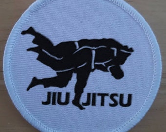 May include: White round patch with a black embroidered image of two people in a jiu-jitsu hold. The text "JIU JITSU" is below the image.