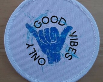 May include: A circular white patch featuring a blue hand gesture and the words "GOOD VIBES ONLY" in black. The patch has a stitched edge and a light blue splatter design.