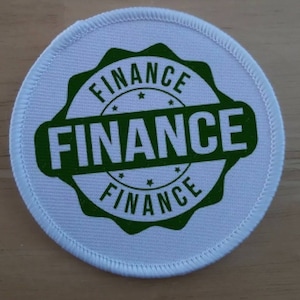 May include: White round fabric patch with a green circular seal that says "FINANCE" in all caps. The word "FINANCE" is repeated three times around the seal.