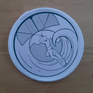 Peut inclure: Patch rond blanc avec un contour bleu. Le patch représente un dessin au trait d'une personne faisant du kitesurf sur une vague.