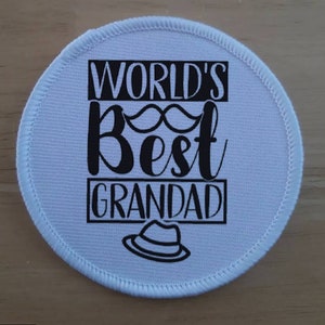 May include: White round fabric patch with black text that reads "World's Best Grandad" with a moustache and a hat graphic.