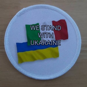 May include: White round patch with the text "WE STAND WITH UKRAINE" and the flags of Ukraine, Italy, and Ireland.