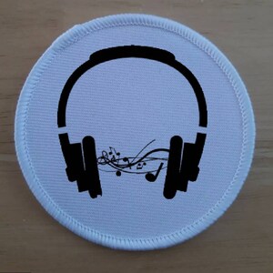May include: White round fabric patch with black headphones and musical notes. The headphones have a black headband and earcups. The musical notes are stylised and flowing.