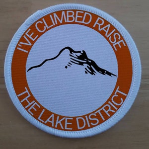 May include: White round patch with an orange border. The patch has a black mountain silhouette and the text "I've Climbed Raise The Lake District".