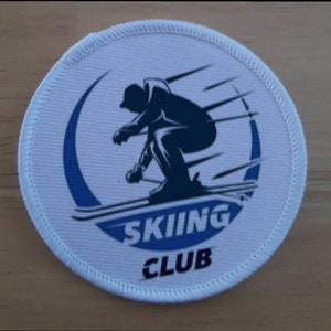 May include: White round patch with a blue circle and a silhouette of a skier in a downhill position. The text "SKIING CLUB" is printed in black below the skier.