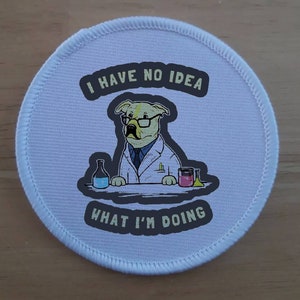 May include: White round patch with a cartoon dog wearing glasses and a lab coat. The dog is holding a beaker and a flask. The text on the patch reads "I have no idea what I'm doing".