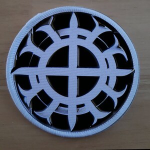 May include: White embroidered patch with a black background. The patch features a white circle with a cross inside, surrounded by a black, stylized, sunburst design.