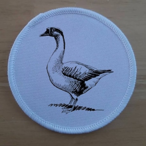 May include: A round, white patch with a detailed black and white illustration of a goose. The goose is standing, with its head and neck curved. The patch has a white stitched border.
