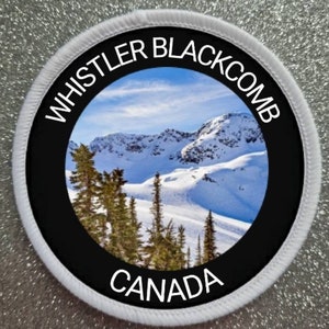May include: A white round patch with black text and a photo of a snowy mountain range. The text reads "Whistler Blackcomb Canada".