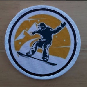 May include: A white round patch with a black outline and a black silhouette of a snowboarder on a snowboard against a yellow background with white snow.