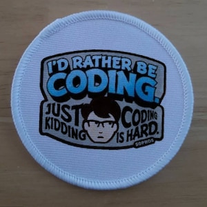Peut inclure: Patch rond blanc avec un graphique bleu et noir qui dit "J'aimerais mieux coder. Je plaisante, coder est difficile." Le graphique comprend également un dessin animé d'une personne portant des lunettes.