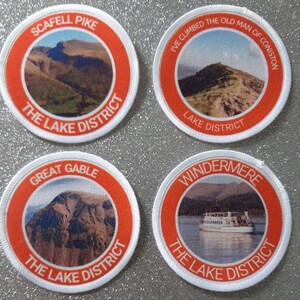 May include: Four round white patches with orange borders. Each patch features a different image of a scenic view from the Lake District in England. The patches have text that reads "Scafell Pike", "I've Climbed the Old Man of Coniston", "Great Gable", and "Windermere".