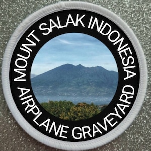 May include: A white round patch with black text that reads "Mount Salak Indonesia Airplane Graveyard" around a circular image of a mountain range.