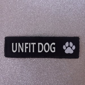 May include: Black fabric patch with white text that reads "Unfit Dog" and a white paw print.