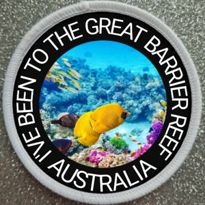 Op de afbeelding: Een ronde witte patch met zwarte tekst die "I've Been To The Great Barrier Reef Australia" luidt. Het midden van de patch toont een kleurrijke onderwater scène met koraal, vissen en blauw water.