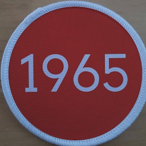 May include: A red circular patch with a white border and the number 1965 printed in white.