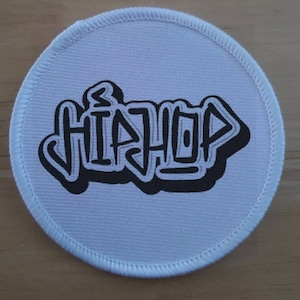 Könnte beinhalten: Runder Stoff-Patch in Weiß mit schwarzem gesticktem Text, der "HIPHOP" in einer Graffiti-Schriftart lautet.