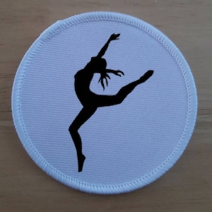 Könnte beinhalten: Runder Stoff-Patch in Weiß mit einer schwarzen Silhouette einer Tänzerin in der Luft.