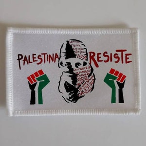 May include: White patch with red and black text that reads "PALESTINA RESISTE". A black and white silhouette of a person with a red and black beard is in the centre. Two black fists with red and green accents are on either side of the silhouette.