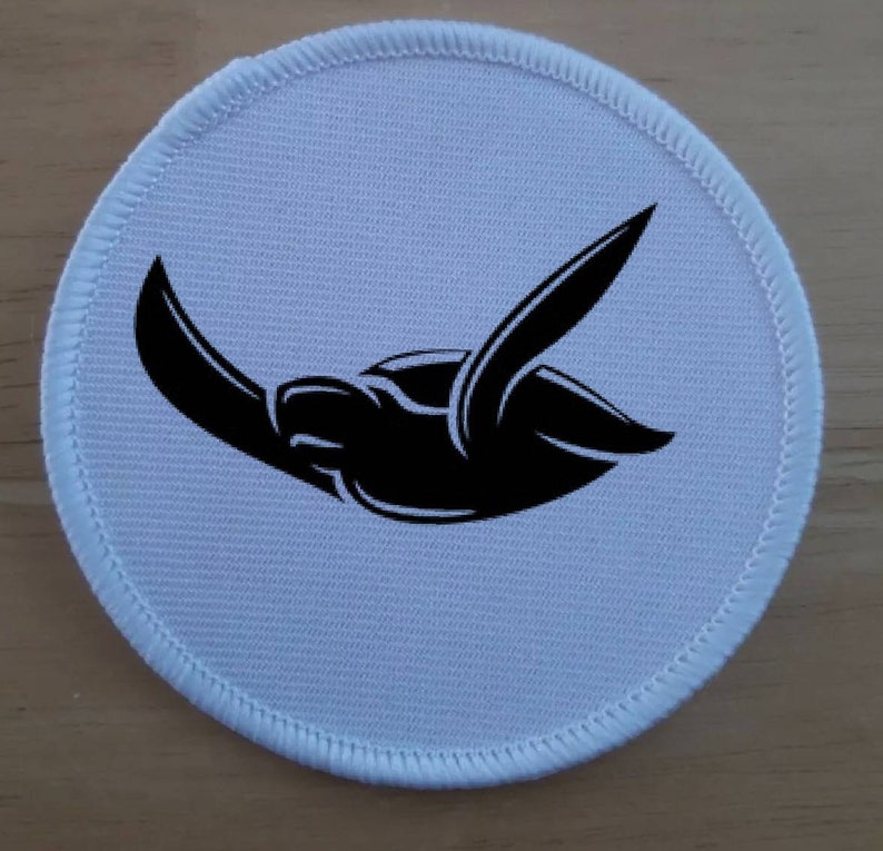 Op de afbeelding: Een ronde witte stoffen patch met een zwart silhouet van een zeeschildpad die zwemt.