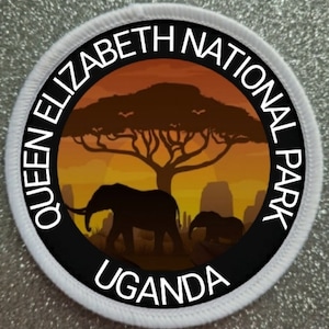Könnte beinhalten: Ein weißer runder Patch mit schwarzem Rand und dem Text "Queen Elizabeth National Park Uganda". Im Inneren des Kreises befindet sich eine Sonnenuntergangsszene mit einem großen Baum und zwei Elefanten in Silhouette.