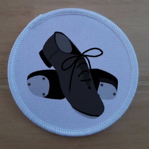 Könnte beinhalten: Ein weißer runder Aufnäher mit einem schwarz-weißen Bild von einem Paar Tanzschuhen. Die Schuhe haben Schnürsenkel und eine schwarze Sohle mit einem weißen Absatz.