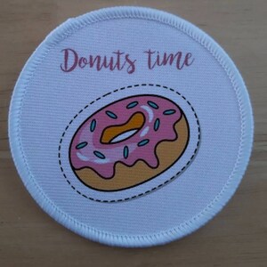 Op de afbeelding: Ronde witte patch met een roze en gele donut met blauwe sprinkles en de tekst "Donuts time" in roze.