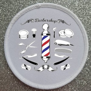 May include: A white round patch with a red, white, and blue barber pole in the center. The barber pole is surrounded by various barber tools, including scissors, razors, combs, and a shaving brush. The text "Barbershop" is written in a stylized font above the barber pole.