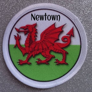 Peut inclure: Un écusson circulaire blanc avec un dragon rouge sur un fond vert et blanc. Le texte "Newtown" est imprimé en noir en haut de l'écusson.