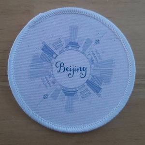 Può includere: Toppa rotonda in tessuto bianco con un design di città blu e bianca e la parola "Beijing" in scrittura corsiva blu.
