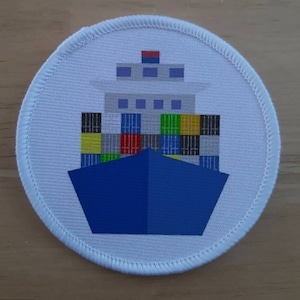 May include: White round patch with a blue and white container ship with colorful cargo containers. The ship has a red and white flag on top.