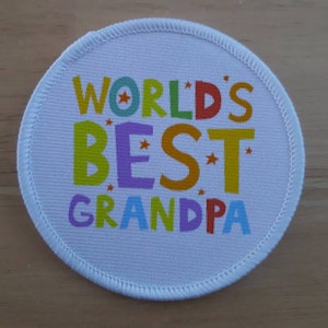 May include: A white round patch with the text "WORLD'S BEST GRANDPA" in colourful letters with stars.