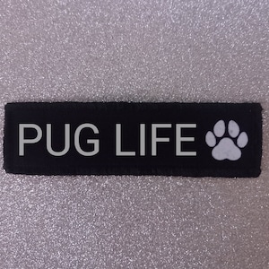 May include: Black fabric patch with white text that reads "PUG LIFE" and a white paw print.